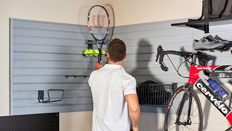 Man hanging tennis racket on slat wall